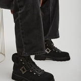 Person wearing black boots and dark jeans sitting on a white chair.