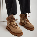 Tan hiking boots with fur trim worn with dark jeans on a light background
