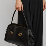 Person holding a black handbag with gold accents on a plain background
