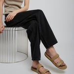 Person wearing beige sandals sitting on a metal stool against a plain background