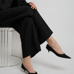 Person wearing a black outfit with wide-leg pants and black shoes on a white background