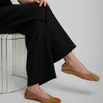 Person wearing black pants and brown shoes sitting on a white surface.