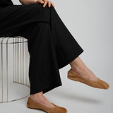 Person wearing black pants and brown shoes sitting on a white surface.