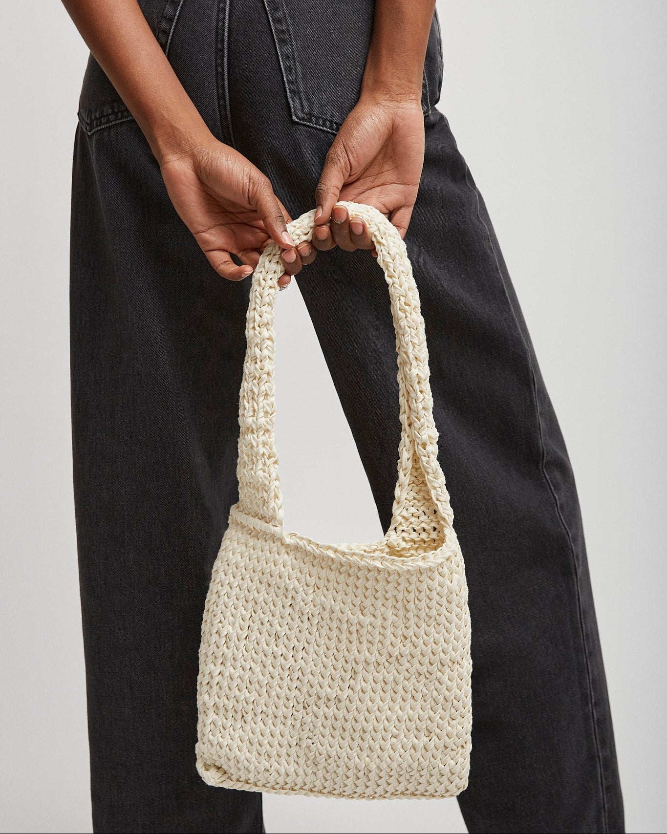 Person holding a woven handbag against a plain background