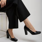 Person wearing black high-heeled shoes and black pants sitting on a chair.