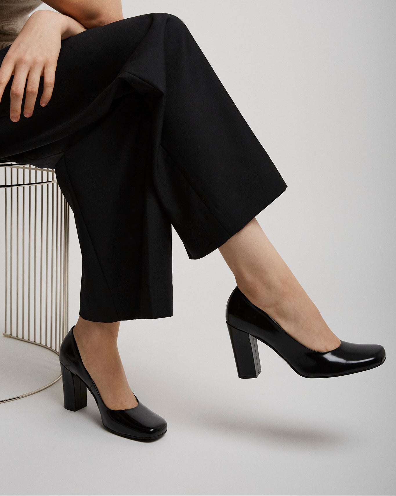 Person wearing black high-heeled shoes and black pants sitting on a chair.