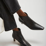 Black ankle boots worn with dark jeans on a light gray background