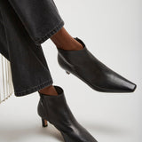 Black ankle boots worn with dark jeans on a light gray background