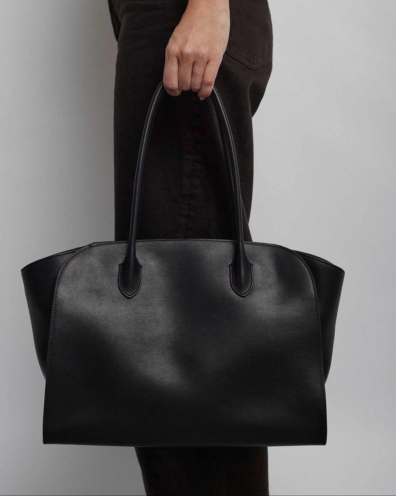 Person holding a black leather handbag against a plain background