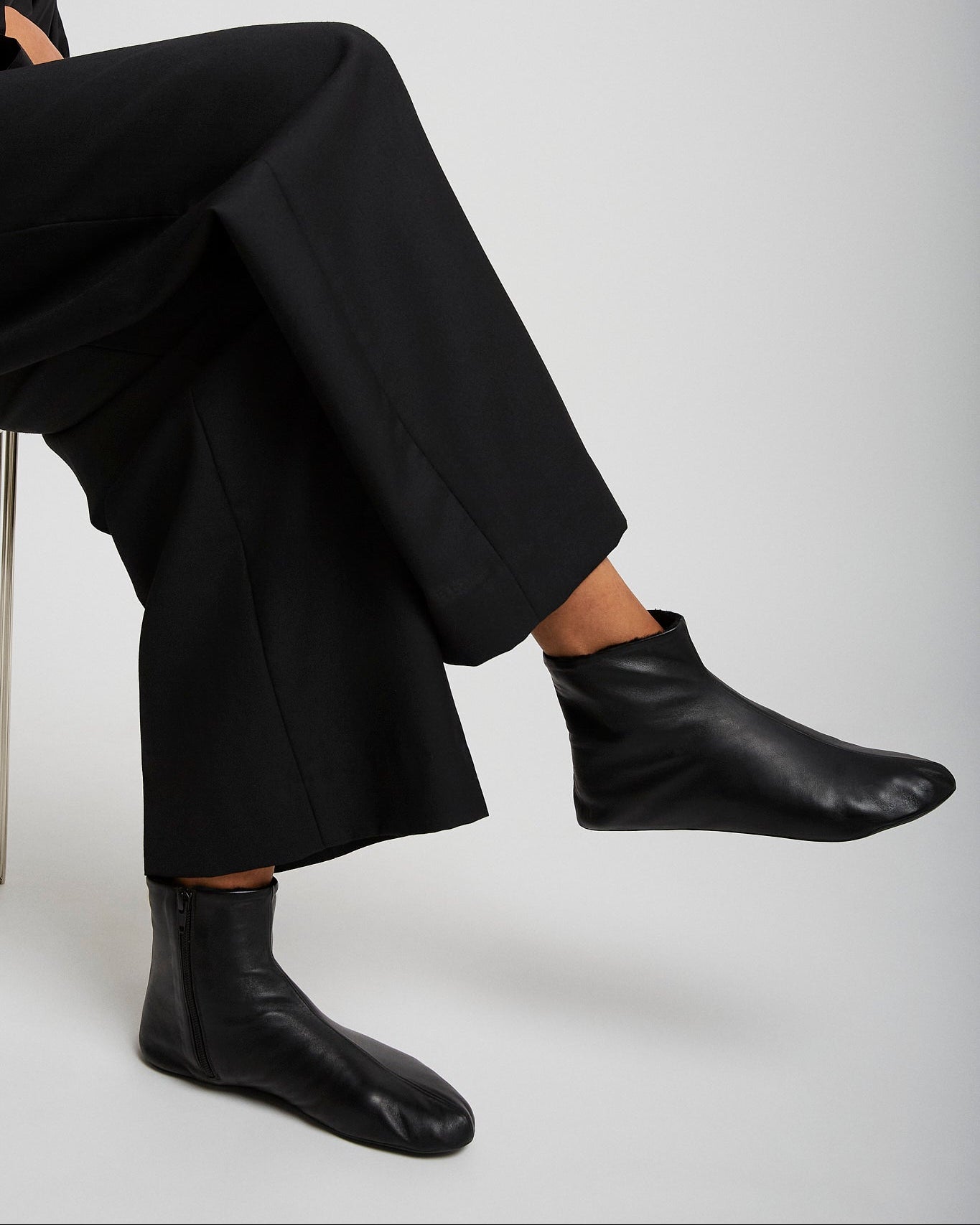Person wearing black leather ankle boots and pants on a white background