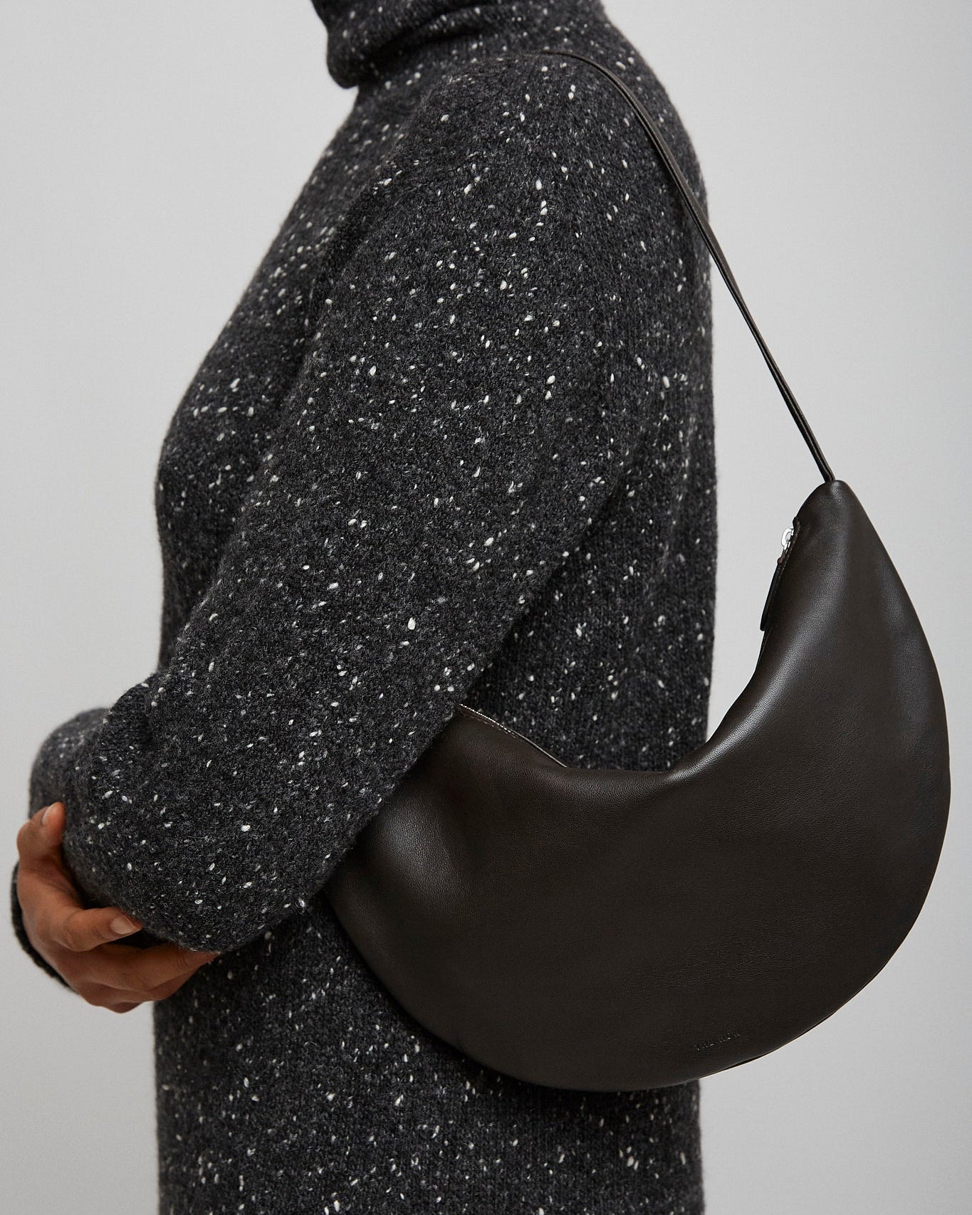 Person wearing a black speckled turtleneck sweater holding a black半月形手袋.