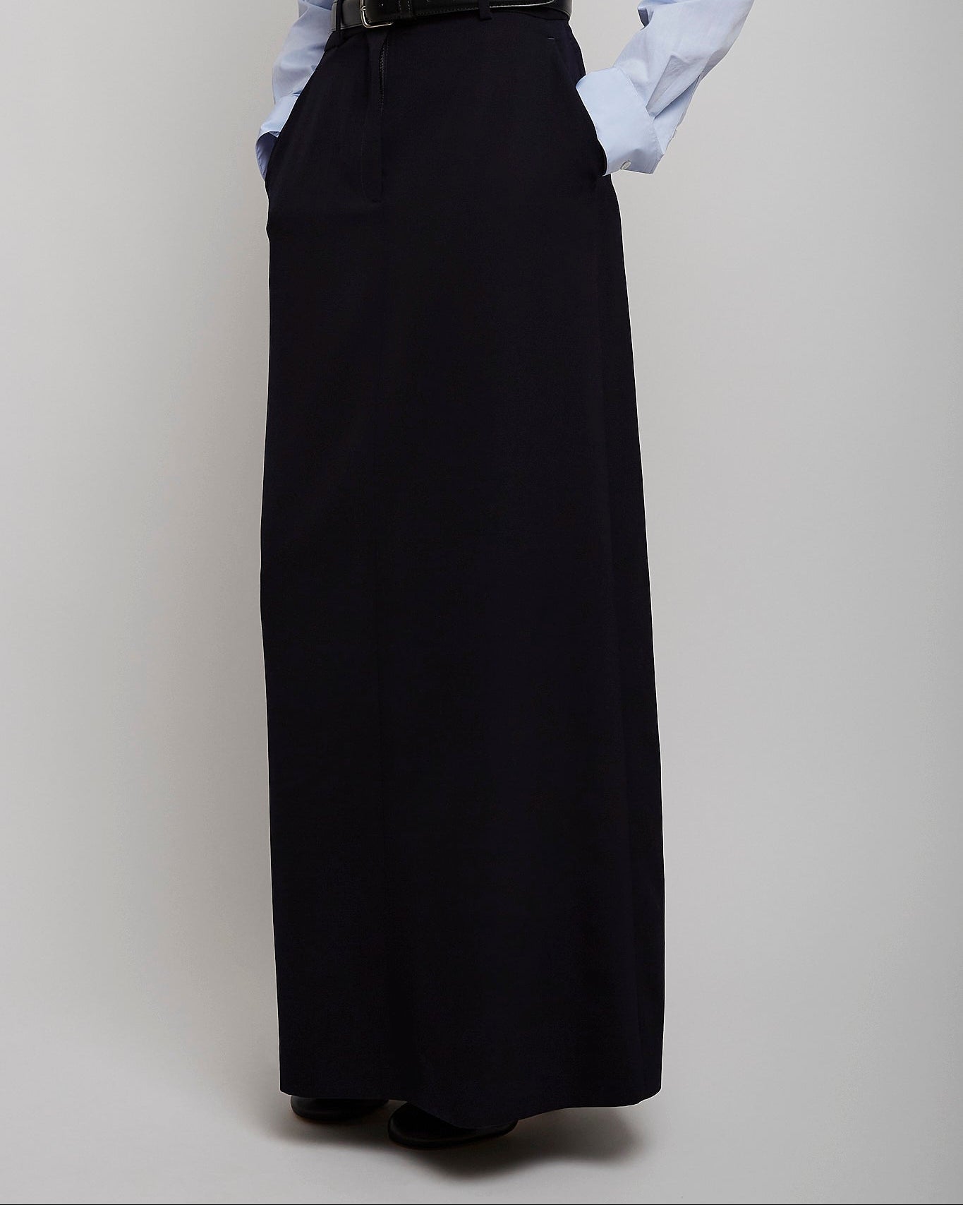 Person wearing a light blue shirt and black long skirt on a plain background