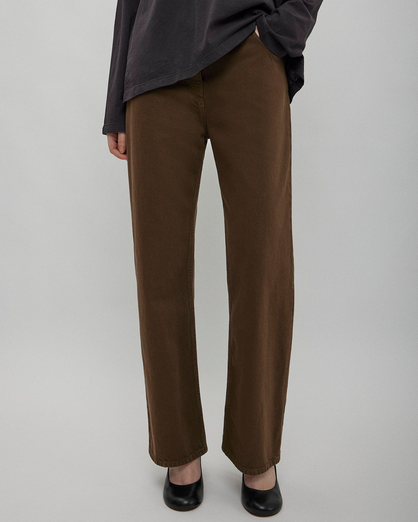 Person wearing brown pants and a dark top on a plain background