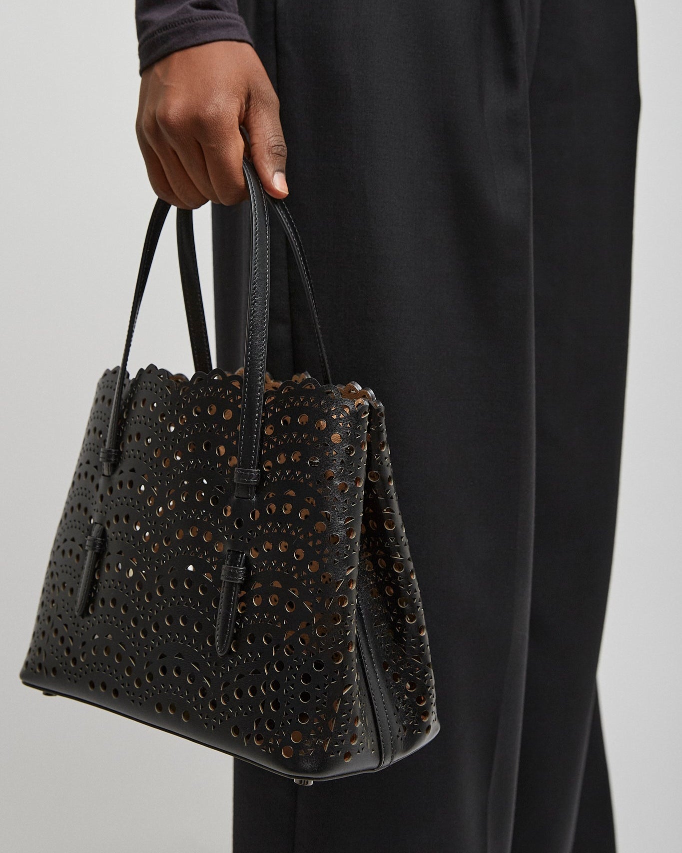 Person holding a black textured handbag against a plain background