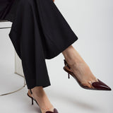 Person wearing black pants and maroon high-heeled shoes on a white background