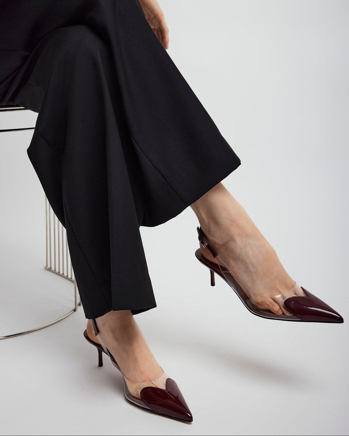 Person wearing black pants and maroon high-heeled shoes on a white background