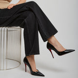 Person wearing black high-heeled shoes with red soles, sitting on a wire stool against a plain background.
