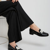 Person wearing black shoes with silver buckles sitting on a white chair.