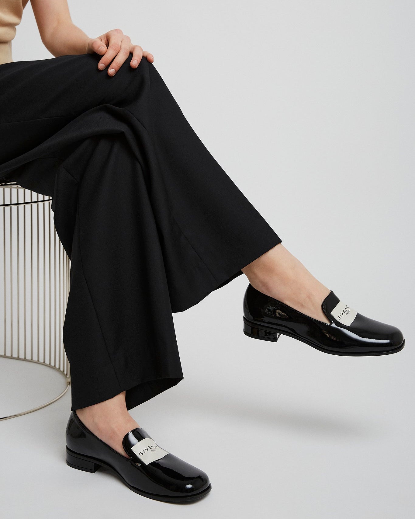 Person wearing black shoes with silver buckles sitting on a white chair.