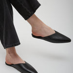 Person wearing black leather mules with black pants on a light gray background