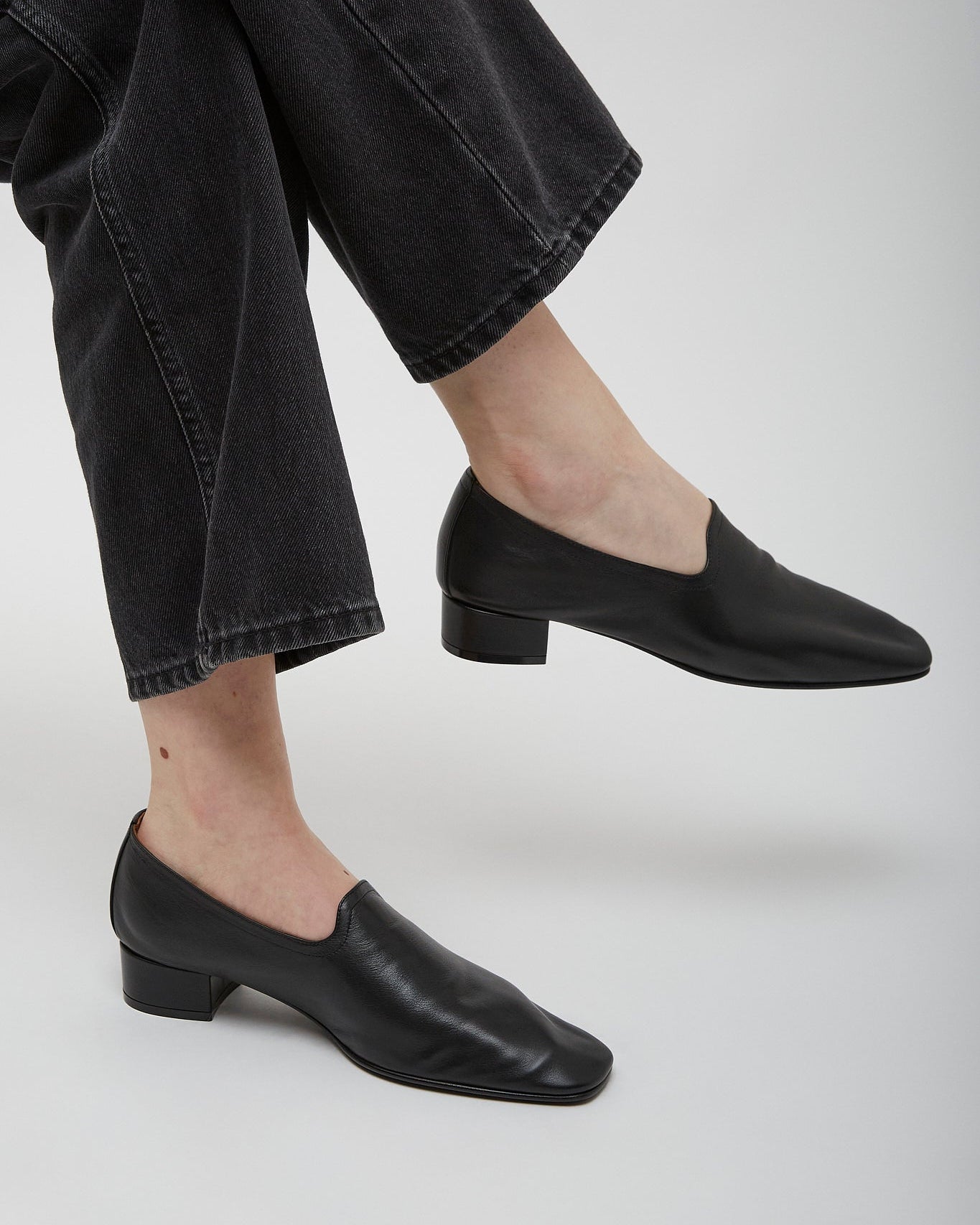 Person wearing black loafers and black jeans on a light gray background