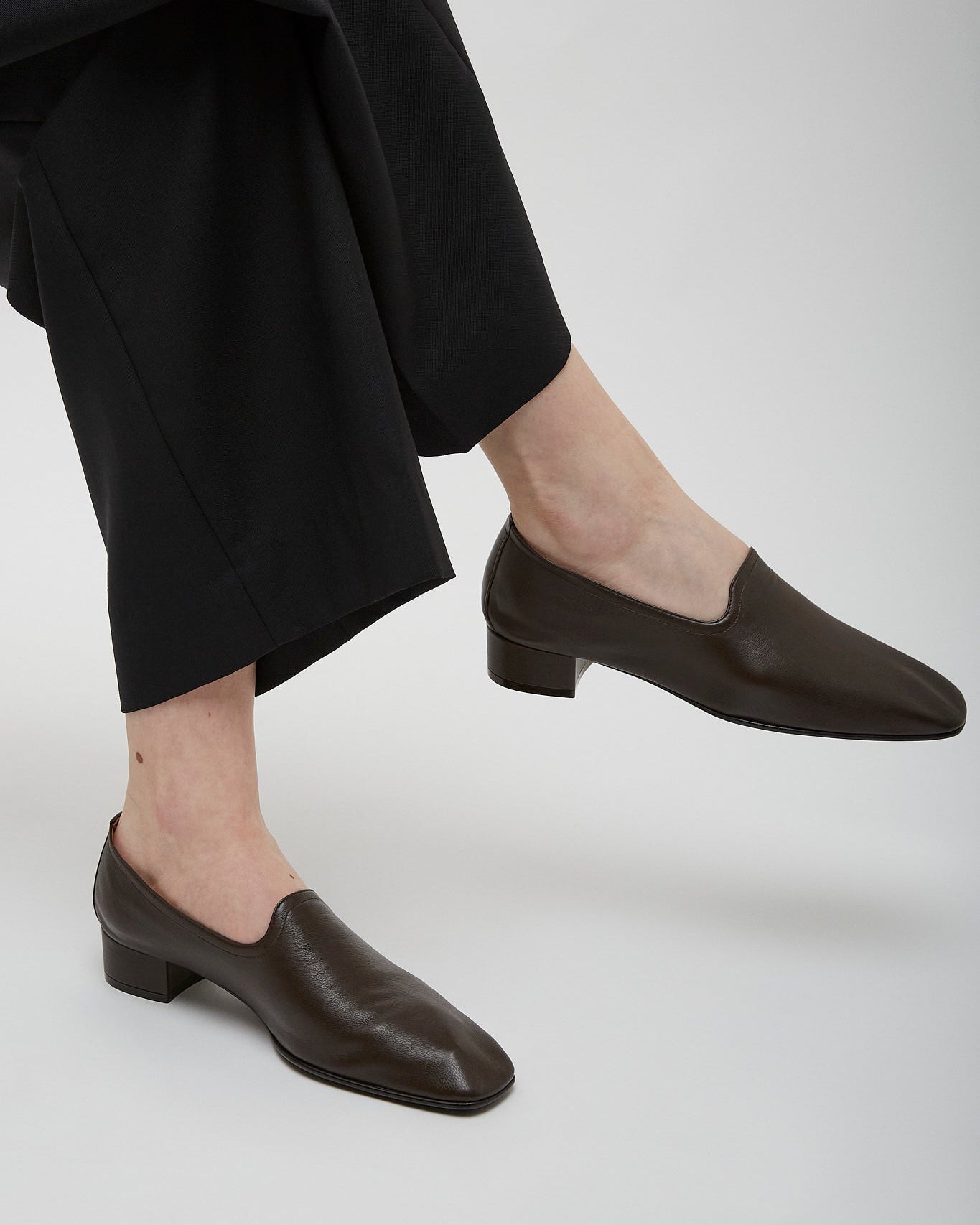 Person wearing brown leather shoes and black pants on a white background