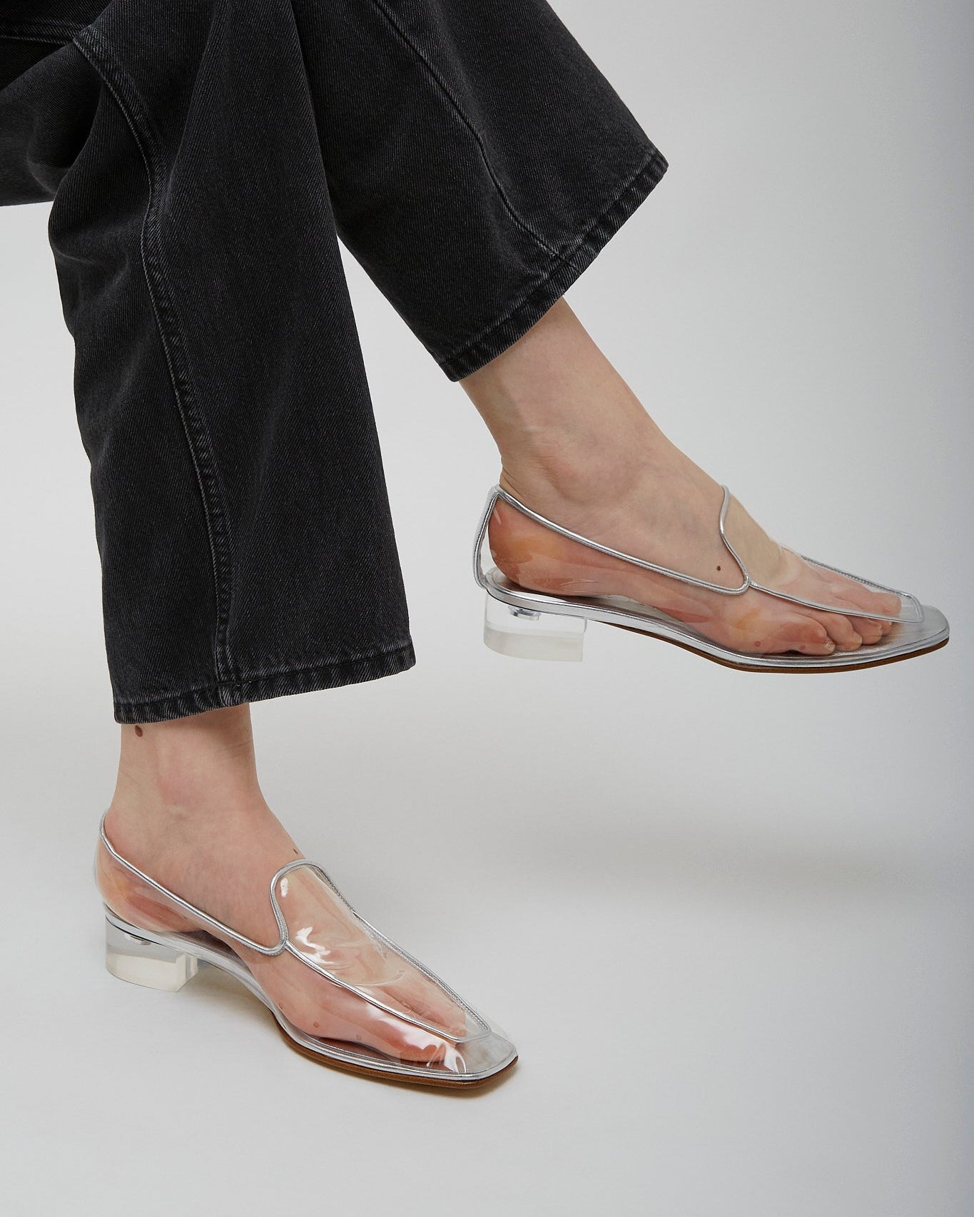 Clear sandals worn with black jeans on a plain background