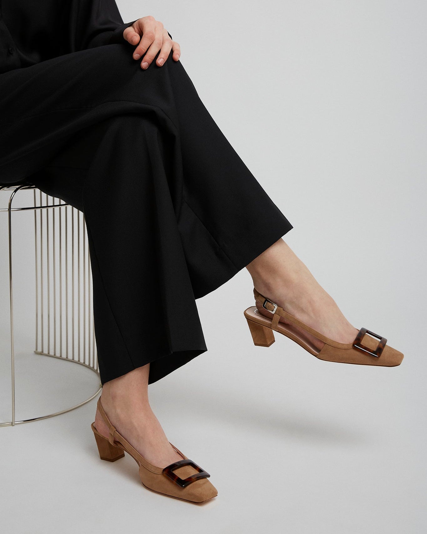 Person wearing black pants and brown shoes with a white background