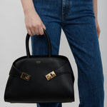 Person holding a black handbag with a gold clasp against a plain background