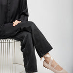 Person wearing black shirt and jeans with beige flats sitting on a white background