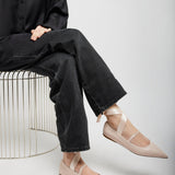 Person wearing black shirt and jeans with beige flats sitting on a white background